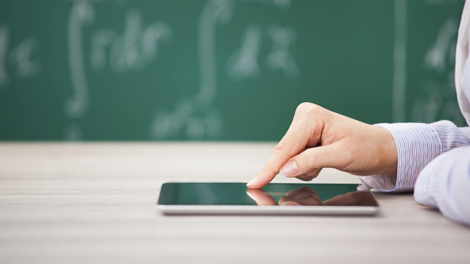 Close-up Of Hand Over Digital Tablet Screen In Front Of Chalkboard