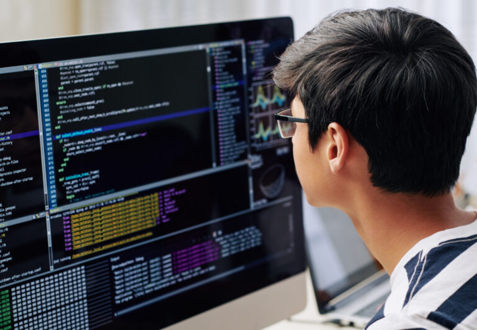 Smart teenage boy in glasses checking programming code on computer screen when sitting at his desk